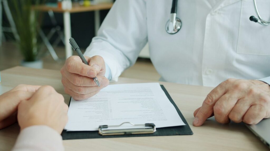 A person reviews health insurance documents beside a phone, treatment notes, and a billing statement.